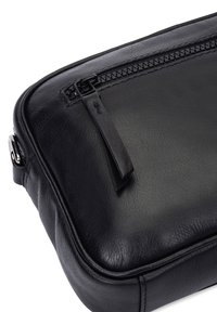 Schwarze Ledertasche mit glatter Oberfläche, einem Reißverschluss mit einem Stoff-Zugband und dezentem Nähen entlang der Kanten.