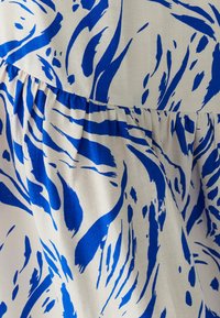 Tissu à motifs bleu et blanc avec des dessins abstraits de coups de pinceau ; texture plissée le long de l'ourlet avec une apparence douce et légère.