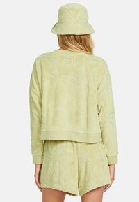 Zelená sada z froté materiálu obsahující texturovanou mikinu a šortky s listovým vzorem, doplněná stylovým kloboukem s širokým okrajem.