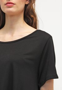 Maglietta nera a maniche corte con scollatura ampia e tessuto in cotone morbido. Il design presenta una vestibilità rilassata e dettagli minimi.
