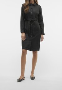 Czarna sukienka z długim rękawem, z guzikiem, z paskiem w talii, kołnierzykiem, bocznymi kieszeniami i gładką teksturą. Charakteryzuje się minimalnym i klasycznym stylem.