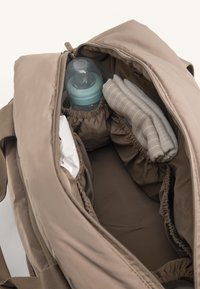 Zaino di tessuto marrone con un ampio interno; include una bottiglia per neonati azzurro chiaro, un panno piegato beige a strisce e tasche elastiche.
