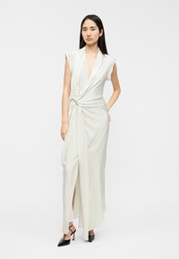 Robe vert clair sans manches avec un décolleté en V profond, un détail noué à la taille et une fente latérale. Tissu lisse et longueur jusqu'au sol.