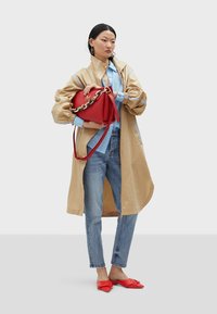 Giacca beige, oversized, con accenti blu, camicia azzurro chiaro, jeans strappati, borsa rossa con tracolle a catena e scarpe ballerina rosse con dettaglio a nodo.