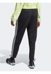 Schwarze Sporthosen mit weißen Seitenstreifen, taillierte Passform, aus glattem Stoff. Getragen mit schwarz-weißen Sneakers.