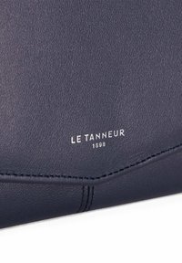 Marineblaue Lederbörse mit strukturierter Oberfläche, ausgestattet mit einem silbernen, gepr Prägin-Logo "LE TANNEUR 1898" auf der Vorderseite und sauberer Naht entlang der Kanten.