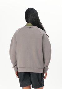 Ljusgrå sweatshirt med avslappnad passform, rund halsringning och ribbad nederkant. Har raglanärmar och en liten hårdvarudetalj på baksidan.