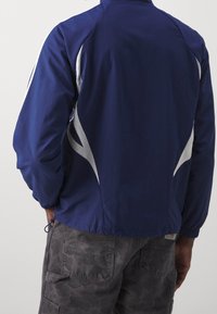 Navy windbreaker jacket featuring white side accents, elastic cuffs, and a drawstring hem. The fabric appears lightweight and textured.