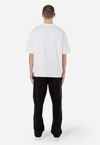 Vit t-shirt med kort ärm och avslappnad passform, i kombination med svarta, löst sittande byxor. Enkel design, slät yta och inga synliga mönster.