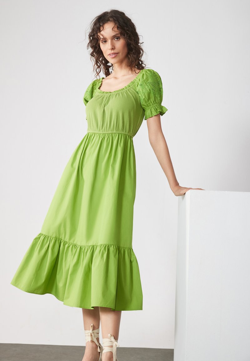 Grünes Baumwoll-Midikleid mit kurzen Puffärmeln, quadratischem Ausschnitt, gerafftem Oberteil und rüschengesäumtem Saum. Glatte Textur mit fließender Silhouette.