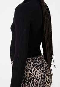 Top negro de manga larga con textura acanalada, combinado con pantalones ajustados de estampado de leopardo que presentan una textura suave y detalles visibles en las costuras.