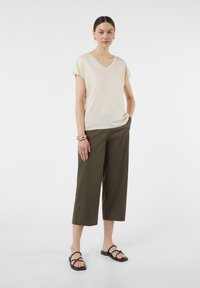 T-shirt beige con scollo a V e maniche corte, abbinato a pantaloni cropped verde oliva e sandali neri con cinturini. Gioielli includono un bracciale dorato.