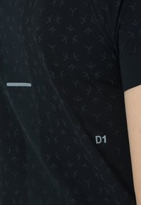 Svart atletisk t-shirt i lättviktig tyg med ett subtilt pilar mönster, en reflexstripa över bröstet och en "D1"-etikett.