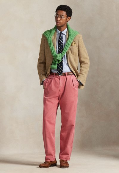 Καφέ σακάκι από τουίντ, πράσινο πουλόβερ δεμένο γύρω από το λαιμό, μπλε πουκάμισο με ρίγες, γραβατα με σχέδια, ροζ παντελόνια, καφέ δερμάτινα παπούτσια.