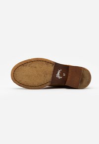 Suola di scarpa in pelle marrone con fondo in gomma marrone chiaro e testurizzato; presenta cuciture visibili e un tacco in legno con un'etichetta di marca sul lato.