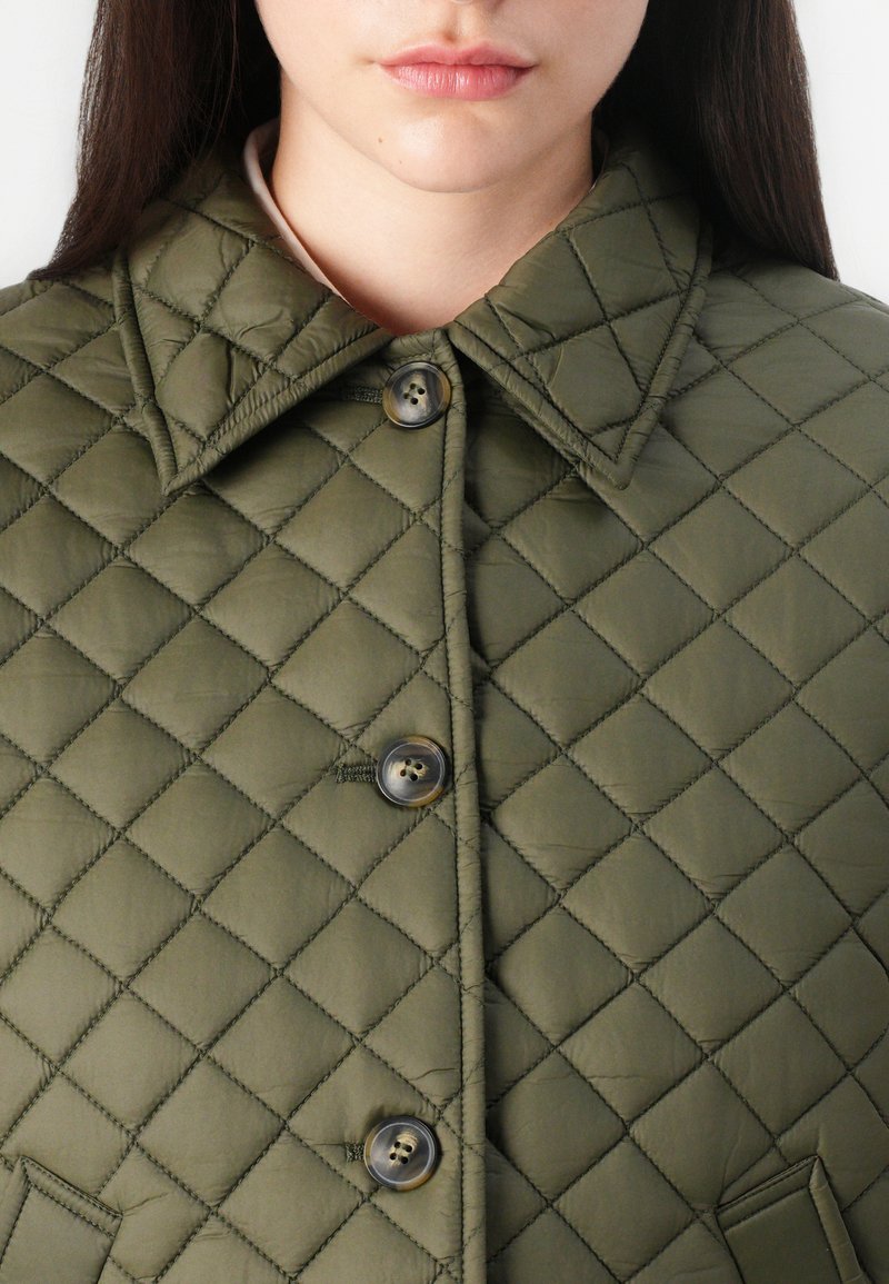 Veste matelassée en vert olive, avec un col structuré, deux boutons et des motifs en diamant sur l'ensemble du tissu.