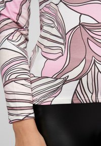 Langarmshirt mit pinkem Blumenmuster und schwarzen Umrandungen. Aus weichem Stoff gefertigt, figurbetontes Design, kombiniert mit einem schwarzen Unterteil.
