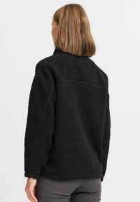 Pull noir en polaire avec un col haut, en matière texturée et douce, à coupe ample ; présente des coutures surpiquées et un ourlet légèrement arrondi.