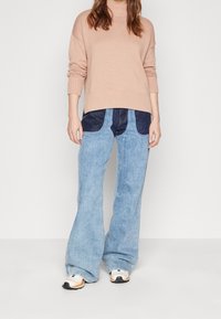 Helles rosa, geripptes Strickpullover kombiniert mit weit geschnittenen, hellblauen Jeans aus Denim, die dunkelblaue Paneele und einen lockeren Schnitt aufweisen.