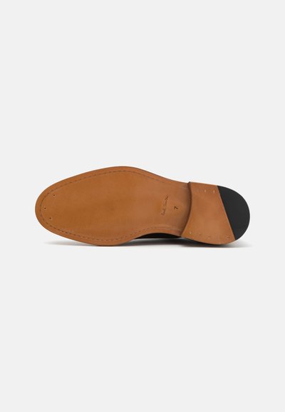 Semelle de chaussure en cuir brun avec une finition lisse couleur tan et un talon en caoutchouc noir. Présente des coutures le long du bord et deux trous près du bout.