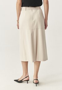 Culottes beige fino al ginocchio con una texture liscia e gambe larghe, caratterizzati da una vita alta e dettagli di cucitura minimi. Indossati con tacchi slingback neri.