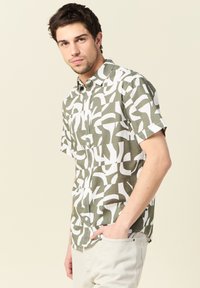 Korte mouwen shirt met een olijfgroene en witte abstracte print; gemaakt van een lichte stof met een knoopsluiting bij de kraag en een borstzak.