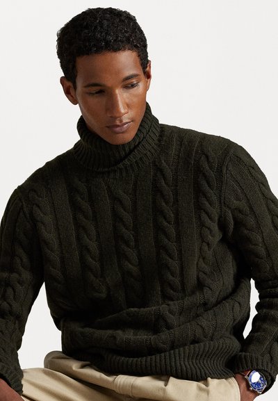 Suéter de cuello alto de punto trenzado color caqui con un patrón texturizado. Cuello y dobladillo acanalados. Combinado con pantalones beige claros.