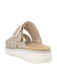 Beige sandal with textured upper, adjustable buckle, and cushioned footbed. Features a white sole with a slight lift and rounded shape.