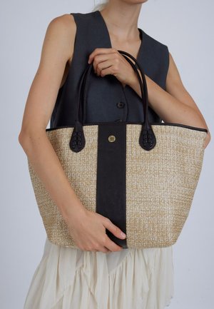 Bež torba-totebag od tkanine s crnim kožnim detaljima, s dvostrukim ručkama i ukrasnim zlatnim gumbom na središnjoj crnoj prugi.