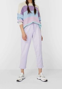 Strickpullover mit pastellfarbenen horizontalen Streifen in Blau, Lila und Creme. Kombiniert mit leichten lila tapered Hosen und weißen Sneakers.