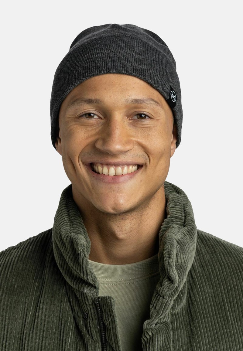 Charcoal knit beanie with a ribbed texture and logo patch. Paired with a green corduroy jacket, featuring a high collar and zipper.