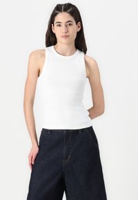 Vit bomullstanktop med ribbad textur och rund halsringning, kombinerad med mörka denimbyxor i vid modell med två framfickor.