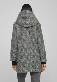 Grey textured coat with an oversized hood, featuring a woven pattern. Long sleeves with black accents, reaching mid-thigh length.