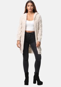 Beige stickad cardigan med huva, kabelmönster, öppen front, långa ärmar, tillsammans med svarta skinny jeans och platåstövlar.