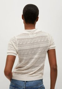 Strick-Polohemd mit kurzen Ärmeln in Creme, ausgestattet mit einem strukturierten offenen Design und einem gerippten Kragen sowie Bündchen.