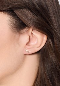 Złote kolczyki w kwiatowym wzorze, z wieloma małymi przezroczystymi kamieniami i gładkimi metalowymi akcentami, które podkreślają kształt ucha.