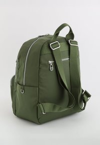 Mochila verde de nylon con correas ajustables acolchadas, bolsillo frontal con cremallera, cremallera en el compartimento principal y bolsillos laterales sobre un fondo liso.