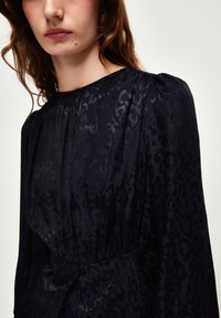 Schwarzes Leopardenmuster-Kleid aus leichtem Stoff, mit langen Ärmeln, plisseeartigem Ausschnitt und tailliertem Detail.