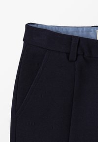 Pantalons tissés bleu marine avec une ceinture lisse, deux poches latérales et une texture subtile. La doublure est bleu clair.