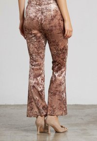 Braun gemusterte Hosen mit floralem Design, samtiger Textur, ausgestelltem Saum und mittlerer Taille, kombiniert mit beigen High-Heels.