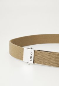 Cintura in tessuto beige con finitura testurizzata, dotata di una fibbia in metallo argentato incisa con "REPLAY" sul davanti.