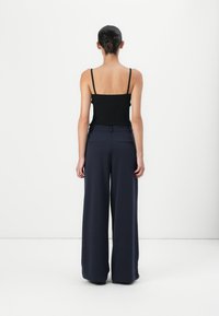Black ribbed tank top paired with navy wide-leg trousers. The outfit features slim straps and a tailored waistband with back pockets.