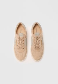 Beige suede sneakers with a textured silver stripe and laces. Rubber sole, rounded toe, and logo detail on the side.