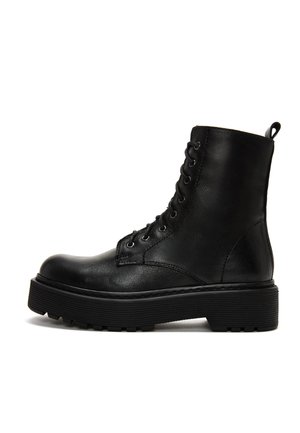 Stivaletto in pelle nera con superficie texturizzata, punta rotonda, occhielli in metallo e suola in gomma spessa. Presenta un tassello sul retro.