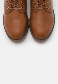 Bottes en cuir marron à lacets avec un bout arrondi, dotées d'œillets en métal et de semelles en caoutchouc texturées pour l'adhérence et la durabilité.