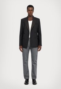 Dubbelzijdig zwarte blazer met satijnen revers, gecombineerd met grijze rechte jeans en zwarte schoenen, met een eenvoudige witte T-shirt eronder.