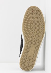 Semelle de chaussure avec motif circulaire en caoutchouc marron clair et nom de marque "ecco" embossé en dessous, tige en tissu noir visible sur le côté.