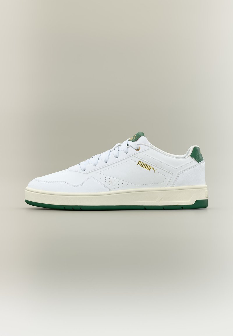 Hvid lavtop Puma-sneaker med grønne accenter, gyldent logo, snørelukning foran og perforerede sidedetaljer på en off-white sål.
