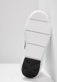 Black sneaker sole with white rubber detailing, featuring horizontal grooves and a textured black section with "KARL LAGERFELD" branding.
