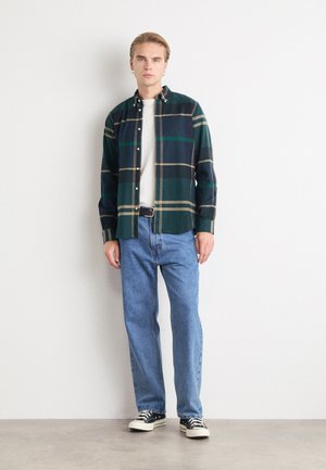 Groene en marineblauwe geruite shirt met knoopsluiting, gecombineerd met lichtblauwe jeans en zwarte sneakers. Het shirt heeft lange mouwen en een kraag.